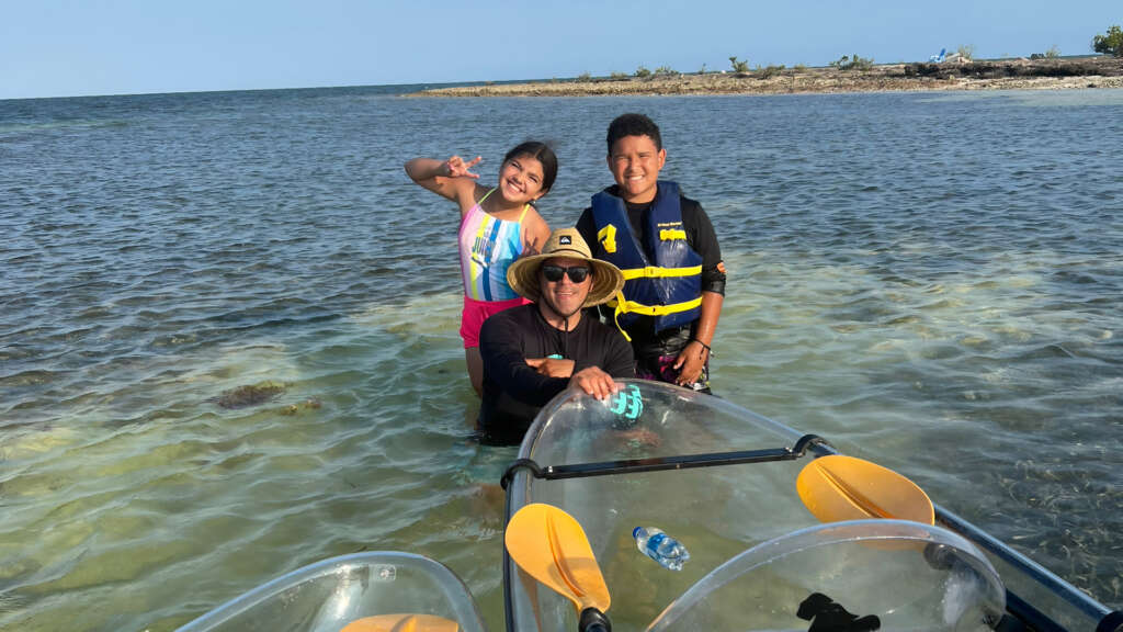 Father and children enjoying crystal clear waters at West Sister Rock sandbar, with Gorilla Boats kayaks and island in background.